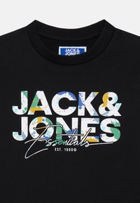 Svart hettegenser med stor, flerfarget grafisk trykk med teksten "JACK & JONES Essentials EST. 1990©" i forskjellige teksturer og mønstre.
