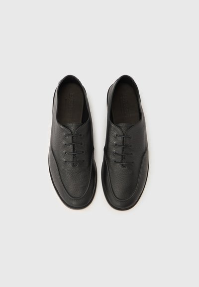 Μαύρα δερμάτινα παπούτσια με υφασμένη υφή, στρογγυλή μύτη και σχέδιο δέσιμου με πέντε οπές. Λείο πέλμα και μινιμαλιστικές λεπτομέρειες.