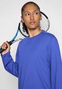 Ilga rankovė purpurinės spalvos sportinė marška su apvalia iškirpte, pasižyminti diskretiniais siūlais ir logotipu "BORG" įspaustu ant krūtinės.