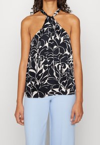 Top halter floreale bianco e nero con collo annodato e tessuto fluido. Abbinato a pantaloni azzurri chiari con texture.