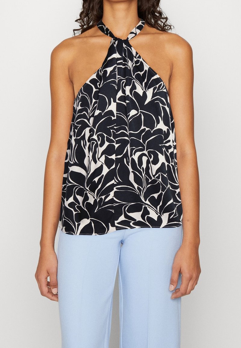 Top halter floreale bianco e nero con collo annodato e tessuto fluido. Abbinato a pantaloni azzurri chiari con texture.