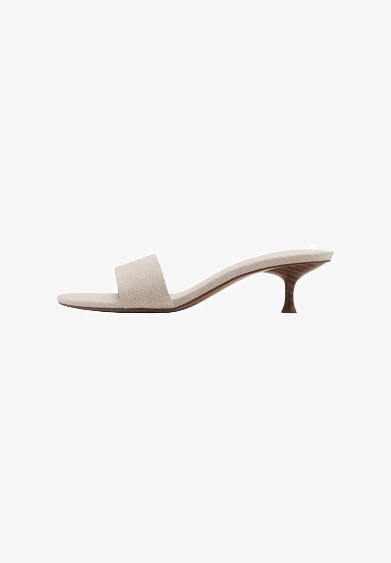 Mule sandale beige à bout ouvert avec une large bride unique et un petit talon aiguilles en bois fin sur fond blanc.