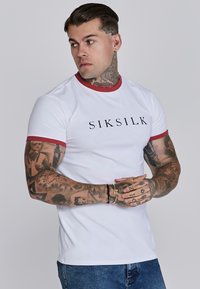 Witte t-shirt met korte mouwen, voorzien van een rode kraag en mouwafwerkingen, met een zwart logo "SIKSILK" over de borst. Gemaakt van katoen.