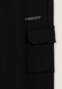 Jogger de algodón negro con diseño de bolsillo doblado. Presenta la palabra "FREDDY" en impresión plateada, añadiendo un detalle de marca sutil.