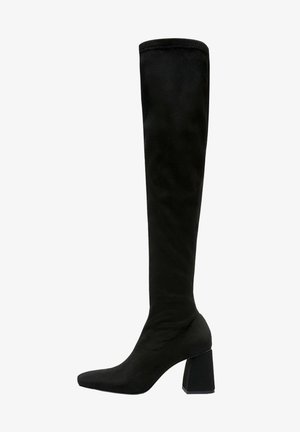 Botte noire montant jusqu'au genou, avec un talon carré, un bout pointu, et un tissu lisse s'étendant juste en dessous du genou.