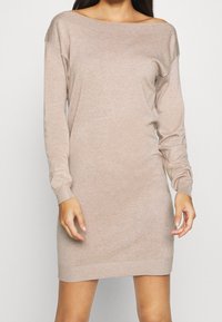 Abito maglione beige a maniche lunghe con scollo off-shoulder, texture morbida, polsini e orlo a coste, e vestibilità rilassata.