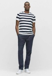 Marinblå och vit randig T-shirt i kombination med mörka byxor; har korta ärmar, rundad halsringning och avslappnade vita sneakers. Enkelt mönster, figurnära stil.