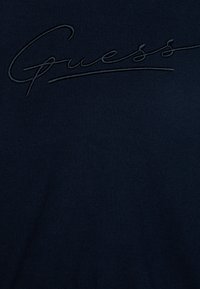 T-shirt blu navy in tessuto morbido con logo "Guess" ricamato in una tonalità più chiara, con una texture liscia e una vestibilità rilassata.
