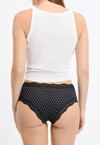 Schwarze Unterwäsche mit weißen Tupfen und Spitzenbesatz, kombiniert mit einem enganliegenden weißen Tanktop. Die Kleidungsstücke haben eine glatte Textur und ein lässiges Design.