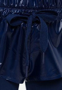 Marinblå glansiga shorts med resårmidja och ett tjockt marinblått snöre knutet i en rosett i mitten fram.