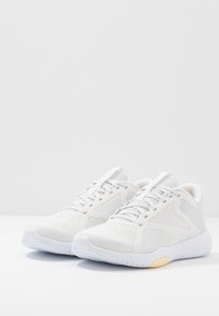 Bílé sportovní boty s horní částí z síťoviny a syntetického materiálu, texturovanou podrážkou a nenápadnými detaily. Mají zaoblenou špičku a zavazování na tkaničky.