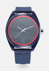 Reloj de pulsera Tommy Jeans azul con anillo rojo en la esfera oscura, manecillas de horas, minutos y segundos en blanco, y correa de tela azul.
