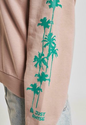 Heller pinkfarbener Pullover mit langen Ärmeln, der grüne Palmen-Graphics entlang des linken Arms und "JUST RHYSE" in der Nähe des Bündchens aufgedruckt hat.