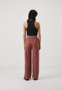 Schwarzes geripptes Crop-Top kombiniert mit hochtaillierten, weit geschnittenen Hosen in einem sanften, staubigen Rosaton mit vertikalen Streifen und strukturierter Baumwolle.