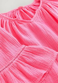 Blusa de algodón rosa con escote en forma de corazón, textura fruncida y mangas acampanadas que presentan un intrincado detalle de encaje a lo largo del dobladillo.