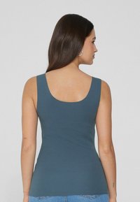 Top ajustado azul sin mangas con escote redondo en la espalda, textura suave y tirantes anchos, combinado con jeans de mezclilla.