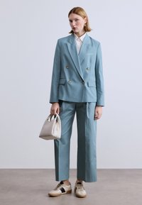 Ανοιχτό μπλε σακάκι διπλής σειράς κουμπιών με αντίστοιχο παντελόνι, σετ με κρεμ τσάντα και μπεζ αθλητικά παπούτσια με μαύρη λεπτομέρεια.