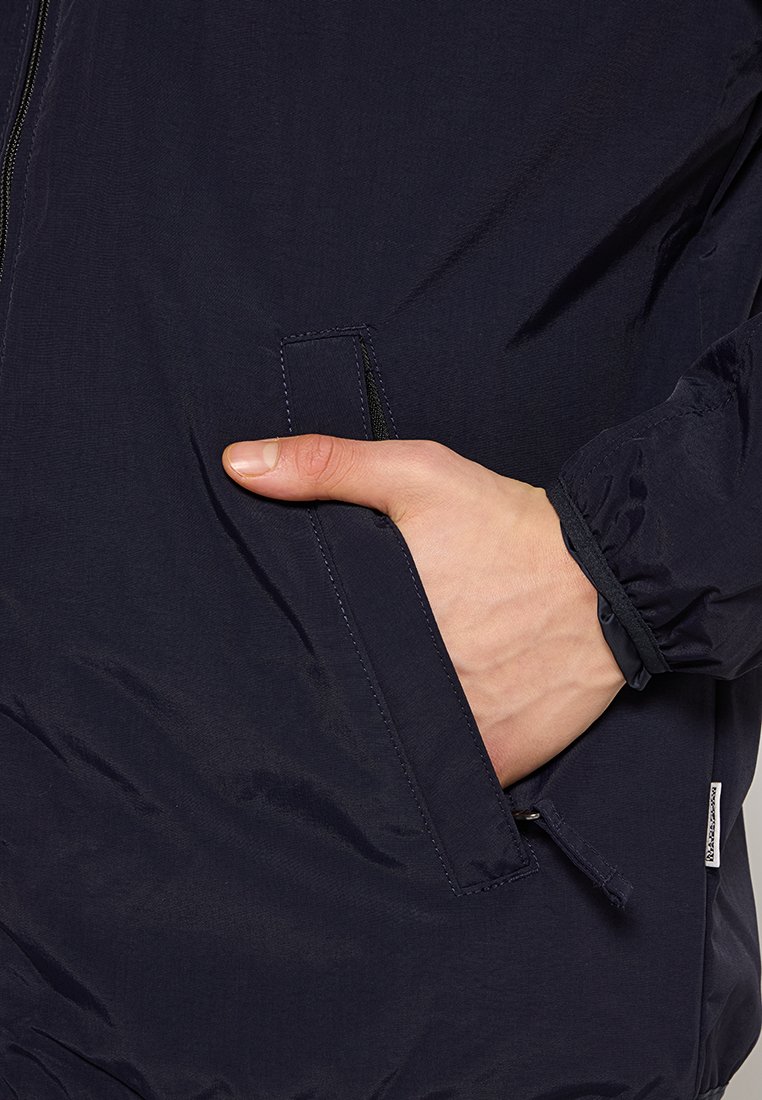 Giacca leggera blu navy con zip, dotata di tasca laterale e finitura testurizzata. I polsini hanno dettagli elasticizzati per un look aderente.