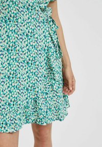 Grön blommig omlottklänning med en volangkant, som har ett strukturerat tyg och en blandning av blå, gula och vita mönster.