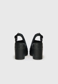 Sandales à plateforme noires avec un dos ouvert, une sangle réglable, une semelle texturée et un matériau supérieur lisse. La hauteur du talon est substantielle avec un design robuste.