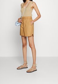 Bruna shorts med elastisk midja och sidofickor, tillsammans med en beige ribbad linne. Bärs med platta sandaletter med remmar. Ljusblå axelväska.