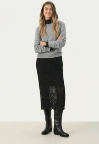 Grauer Pullover mit langen Ärmeln, über einen schwarzen Spitzenrock geschichtet. Der Rock hat ein Blumenmuster und reicht bis zur Mitte der Wade, kombiniert mit schwarzen knielangen Stiefeln.