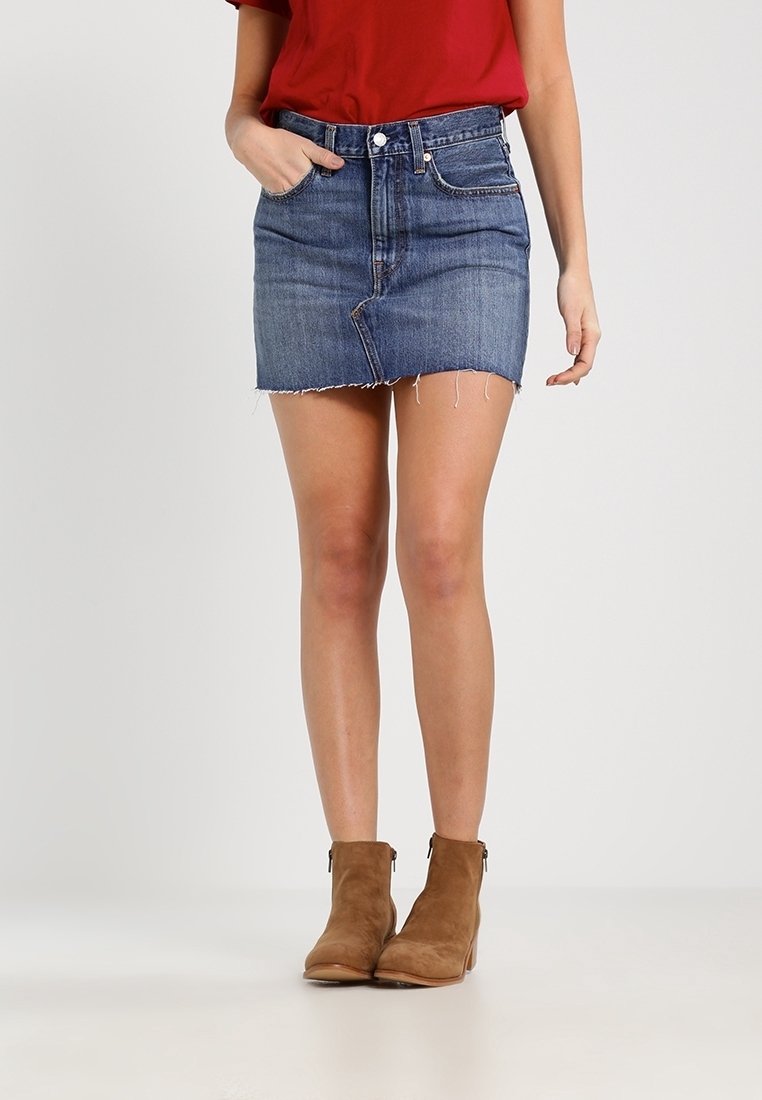 Denimkjol med fransar i nederkant, i en ljus till medelblå tvätt, fem fickor och midjehöjd, tillsammans med bruna ankelstövlar.