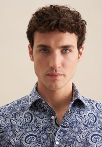 Granatowa koszula w wzór paisley z kołnierzykiem na guziki, z białymi akcentami i gładką teksturą materiału. Zbliżenie na wzór.