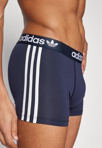 Navy blue cotton boxer shorts with a white three-stripe design on the side and an elastic waistband featuring the Adidas logo.