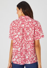 Camicia a maniche corte con un motivo floreale rosso e bianco, design con colletto e vestibilità rilassata con dettaglio a pieghe sul retro.