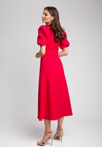 Czerwona midi sukienka z bufkami i dopasowanym wcięciem, z gładką fakturą i rozkloszowanym dołem, uzupełniona cielistymi sandałami na wysokim obcasie.
