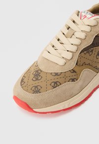 Beżowy tenisówka zamszowa i z wzorzystej tkaniny. Okrągły nosek, kremowe sznurowadła i czerwona gumowa podeszwa. Logo nadrukowane na boku i języku.