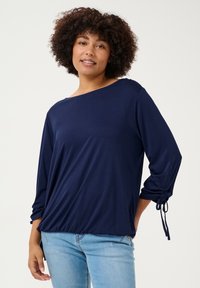 Haut à manches longues bleu marine en tissu lisse, avec une coupe décontractée, un col bateau et des poignets à cordon réglable.