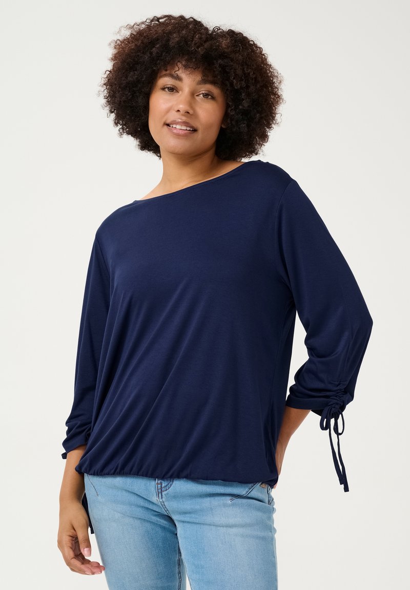 Haut à manches longues bleu marine en tissu lisse, avec une coupe décontractée, un col bateau et des poignets à cordon réglable.