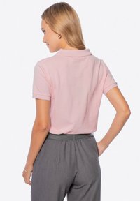 Světle růžová polo tričko s límečkem, krátkými rukávy a ribbovanou texturou, spárované s šedými volnými kalhotami s vysokým pasem.
