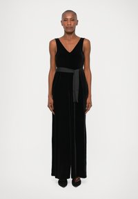 Mono de terciopelo negro con escote en V, diseño sin mangas y un cinturón de tela a juego en la cintura. Silueta de pierna recta y acampanada.