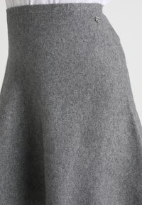 Grauer Wollrock mit schwingendem Design, der eine subtile Textur aufweist und einen dekorativen silbernen Knopf am Bund hat.