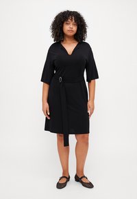 Černé šaty s výstřihem do V, krátkými rukávy a páskem v pase s stříbrnou sponou. Hladká látka, délka ke kolenům a volný střih.