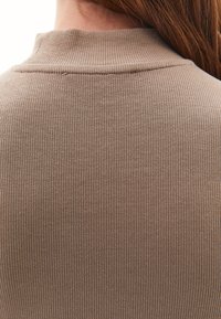 Prążkowany, dopasowany sweter w stonowanym odcieniu taupe z wysokim kołnierzem. Materiał jest gładki, z pionowymi liniami, zapewniającym obcisłe dopasowanie.