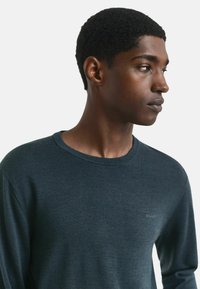 Pull bleu marine à col rond, fabriqué dans un matériau lisse. Il présente un logo subtil sur la poitrine et une coupe décontractée.