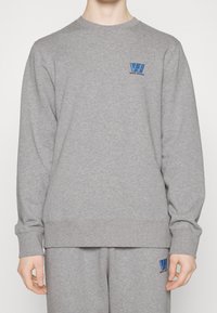Grå sweatshirt i en bomullsblandning, med rund halsringning, långa ärmar och en blå logotyp på vänster bröst.