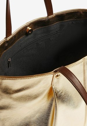Una borsa tote dorata lucida con manici marroni, aperta per rivelare un interno nero e una tasca con cerniera lungo il lato.