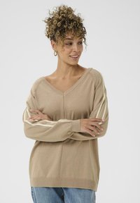 Beige Strickpullover mit V-Ausschnitt, langen Ärmeln und weißen vertikalen Streifen auf den Schultern. Weicher Stoff und lässige Passform.