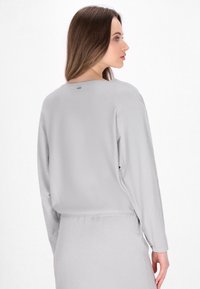 Lichtgrijs langmouwtop met een relaxte pasvorm, ronde hals, subtiele textuur en een klein labeldetail aan de achterkant.