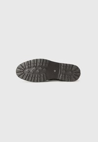 Suela de zapato de goma negra con surcos y dibujos profundos. Presenta una forma redondeada y marcas de tamaño cerca del talón.