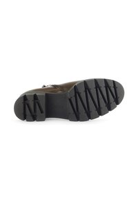 Semelle de botte en cuir marron avec un motif de gomme noire texturée. Présente des rainures angularies et un détail de marque en relief.