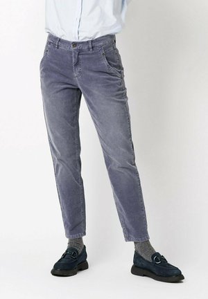 Person wearing gray corduroy pants, gray socks, navy blue loafers, and a light blue tucked-in shirt on a plain background.