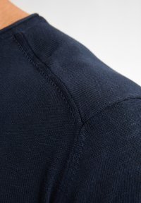 Marinblå stickad crew neck-tröja som visar en närbild på axelsömmen med en jämn textur och fina sömnadsdetaljer.