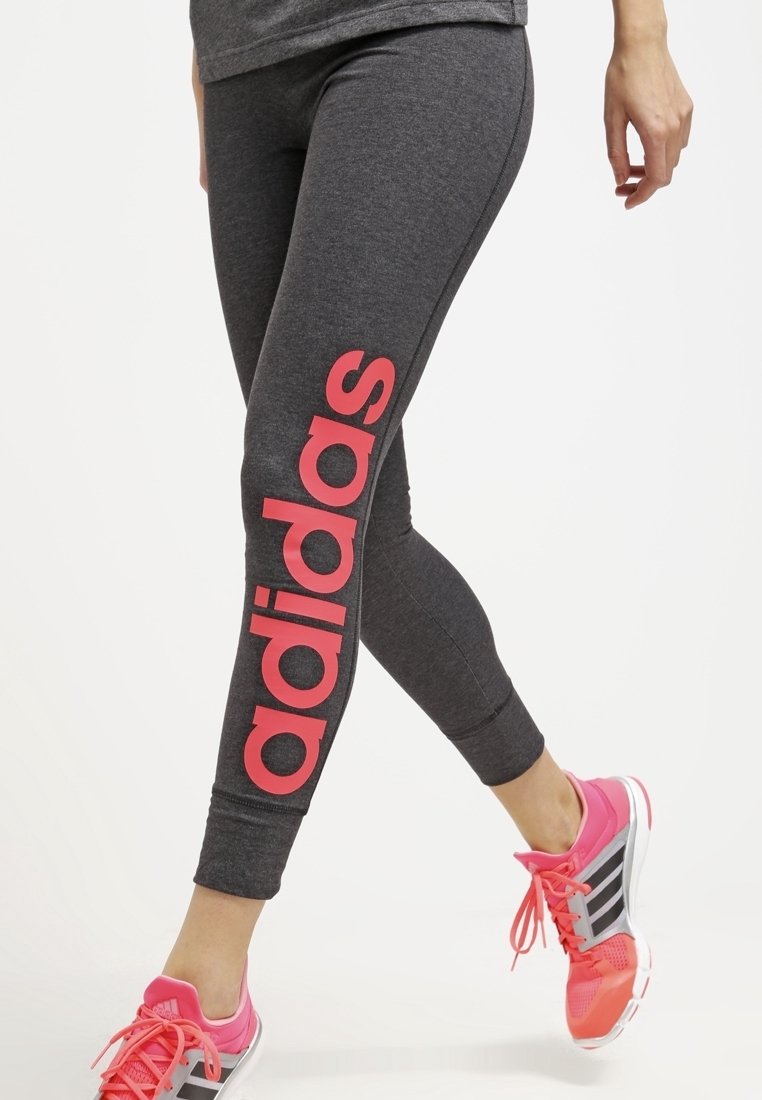 Grå leggings med en stor rosa "adidas"-logotyp längs vänster sida, med en kroppsnära design och slät yta, ihopparade med ljusrosa träningsskor.