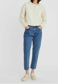 Sweat à capuche zippé de couleur crème avec un tricot texturé, associé à un jean droit taille haute bleu clair et des baskets beiges.